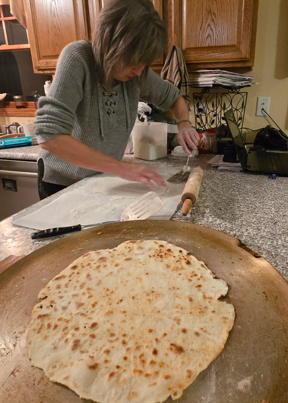 lefse on the griddle with me attempting to loosen it from the parchment paper.